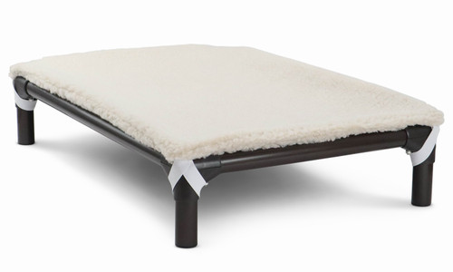 Cream color fleece accessory pad shown on top of a pvc bed, the pad is held to the bed by elastic straps that hook each the legs of the bed